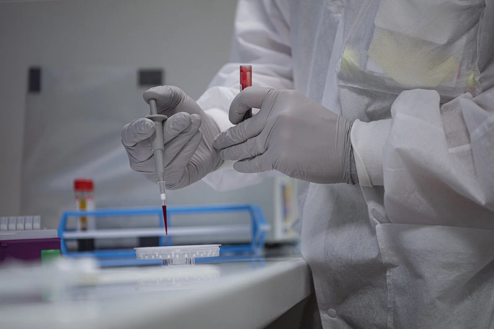 Suojapukuinen laboratoriotyöntekijä käsittelee näyteputkea